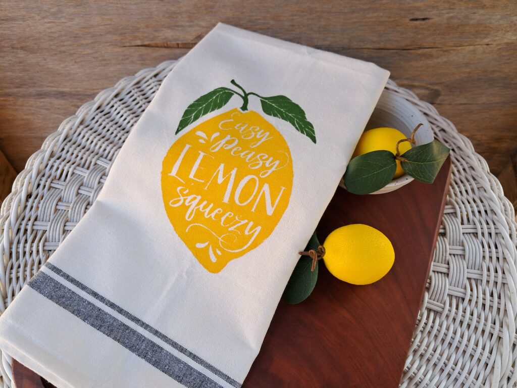 Finished lemon tea towel on a wooden cutting board styled with two lemons.